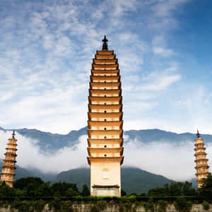 三座石塔高聳入雲，背景是霧氣繚繞的山巒和部分多雲的天空。 — 美學雲朵 壁紙