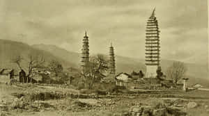 三座歷史悠久的塔樓矗立在一個有石屋和光禿樹木的山村中。 — 復古 壁紙