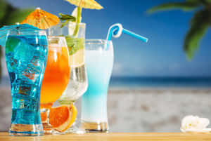 沙灘桌上三杯色彩繽紛的熱帶飲品，附有傘。 — 海灘 壁紙
