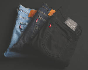 三條摺疊的Levi's牛仔褲，不同洗水，放在深色表面上。 — 丹寧 壁紙