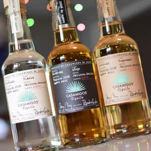 三瓶 Casamigos 龍舌蘭酒，背景有色彩繽紛的模糊燈光。 — 品牌 壁紙