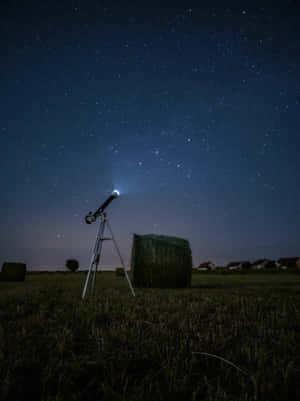 田野中的望遠鏡，下方是星空，附近有乾草捆。 — 星星 壁紙
