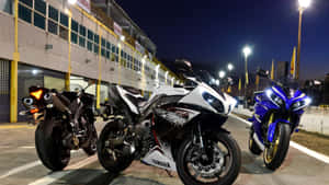 三輛Yamaha跑車在夜間停放在賽車設施外，在明亮燈光下。 — iMac 壁紙