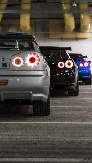 三輛改裝跑車帶有發光的尾燈，停放在地下停車場。 — 日產 Skyline GTR R34 壁紙