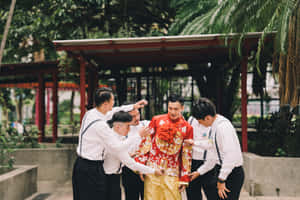 伴郎在亭子下協助穿著傳統紅金色婚禮服飾的新郎。 — 慶祝 壁紙