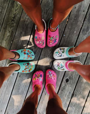 五個人穿著帶有貼紙的彩色Crocs，在木甲板上圍成一個圓圈站立。 — 夏日美學動畫 壁紙