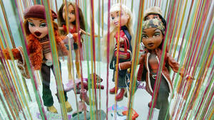 五個穿著時尚服裝的 Bratz 公仔在色彩繽紛的懸掛線後面。 — 玩具總動員叉奇 壁紙