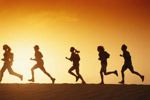 五個人在日落時分在沙灘上奔跑，身後是橙色的天空。 — Running 壁紙