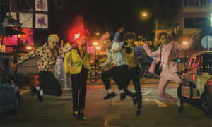 五名身穿色彩繽紛西裝的男子在夜間霓虹燈照亮的街道上充滿活力地跳舞。 — 宇宙 壁紙