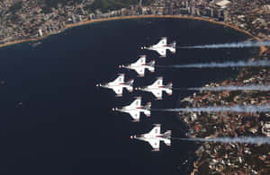 五架戰鬥機以編隊飛越沿海城市，帶有煙跡。 — 海洋桌面 壁紙