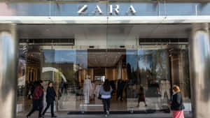 購物者經過一間Zara服裝店，玻璃門和內部展示清晰可見。 — Zara 壁紙