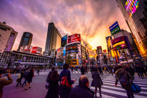 日落時分，行人穿過東京繁忙的十字路口，頭頂霓虹燈閃爍。 — MacBook Pro M4 壁紙