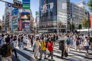 行人穿過東京一條繁忙的街道，有高樓大廈和明亮的招牌。 — 東京 壁紙