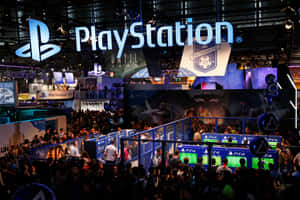 PlayStation遊戲展上的人群，伴隨著發光的標誌和主機。 — MacBook Pro M2 壁紙