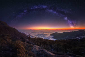山峰在星空下升起於雲海之上，伴隨著銀河 — 日落 壁紙