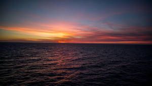 海洋日落，鮮豔的橙色和粉紅色雲彩倒映在黑暗的水面上。 — 海景 壁紙
