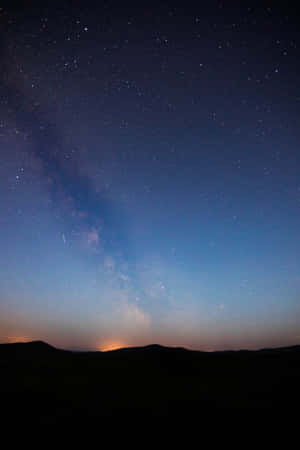 暮色中黑暗山丘上的銀河系，星空與溫暖的地平線光芒。 — 小米平板 9 Pro 壁紙