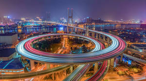 夜間發光的螺旋形高速公路，車燈流光，背景是城市天際線。 — 塔橋 壁紙