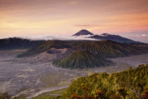 日出時分的火山山脈，有雲朵和綠色植被。 — 黎明 壁紙