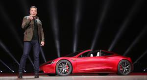 伊隆·馬斯克在燈光舞台上展示一輛紅色Tesla Roadster。 — 伊隆·馬斯克 GIF 壁紙