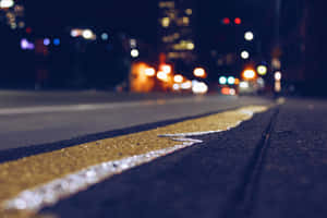 夜晚濕漉漉的黃色道路標線，背景是模糊的城市燈光和車流。 — MacBook Air M4 壁紙