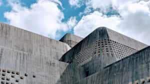 粗獷主義混凝土建築，具有幾何形狀和穿孔牆壁，背景是藍天白雲。 — 博物館 壁紙