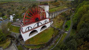 綠色山谷中白色建築上的紅色水車與石砌高架橋 — 秋季 壁紙