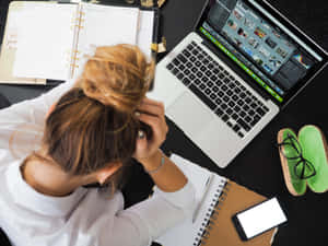 女性在雜亂的辦公桌上使用筆記型電腦、筆記本和電話，工作壓力大。 — 讀書 壁紙