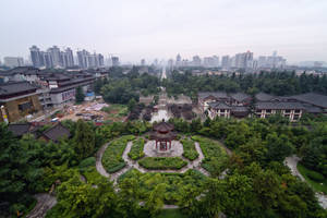 傳統中式花園亭台樓閣，周圍環繞著綠植，背景是現代城市天際線。 — 3:2 壁紙