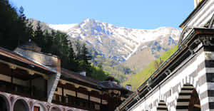 帶有條紋拱門的修道院建築俯瞰著藍天下的積雪山峰。 — 山脈 壁紙