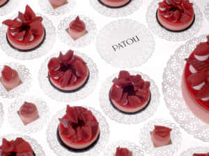 Patou品牌甜點，白色蕾絲墊布上飾有紅色花瓣。 — 烘焙坊 壁紙