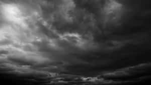 濃密的烏雲在戲劇性的單色光線下旋轉。 — 簡約暗黑美學 壁紙