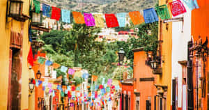 色彩繽紛的 papel picado 橫幅懸掛在節日街道的殖民建築之間。 — 墨西哥 壁紙