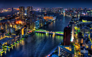 夜間城市天際線，燈火通明的建築物和水面上發光的橋樑。 — 東京 壁紙