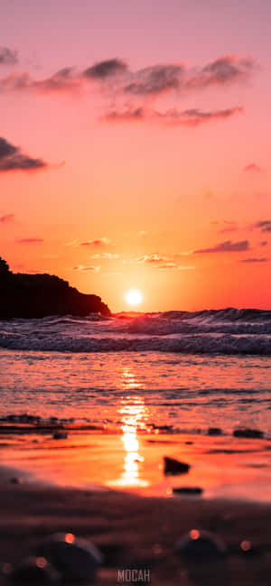夕陽映照海洋，海浪拍打岩石海岸 — iPhone 16 壁紙