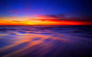 充滿活力的夕陽色彩在黃昏時反射在平靜的海浪上。 — Chill 壁紙