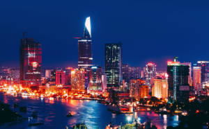 夜間城市天際線，帶有發光的建築物和河流倒影。 — 胡志明市 壁紙