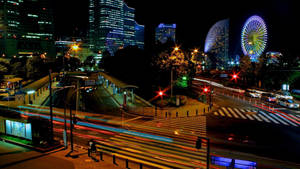 夜間城市景觀，發光的建築物和摩天輪，汽車燈光軌跡。 — 日本 壁紙