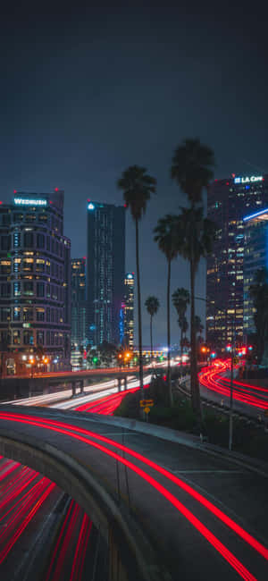 夜晚的城市，棕櫚樹和移動車輛的紅色光軌。 — Moto E 壁紙