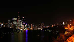 夜間城市天際線，發光的建築物倒映在河流中。 — 黑暗城市 壁紙