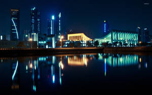 夜間城市天際線，發光的建築物倒映在水中。 — 科威特 壁紙