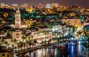 沿海城市的夜景，沿運河有燈火通明的建築物和棕櫚樹。 — 城市 壁紙
