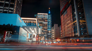 夜晚的城市街道，有明亮的建築物和移動車輛的光軌。 — 城市 壁紙