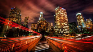 夜晚的城市，有燈火通明的摩天大樓和汽車留下的紅色光軌。 — 洛杉磯 壁紙