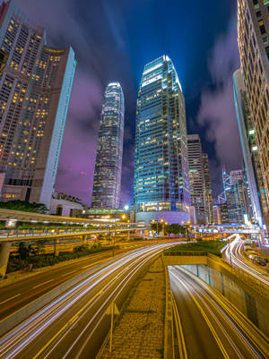 夜間城市場景，有燈火通明的摩天大樓和流動的車燈。 — 城市燈光 壁紙