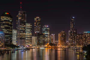 夜間城市天際線，燈火通明的摩天大樓倒映在水面上。 — 阿德雷德 壁紙