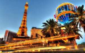 拉斯維加斯夜晚，棕櫚樹下有艾菲爾鐵塔複製品和熱氣球雕塑，帶有燈光軌跡。 — 阿德雷德 壁紙
