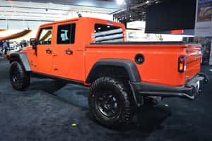 橙色Jeep皮卡車在車展上展出，配備黑色輪胎和堅固設計。 — Surface Pro 壁紙
