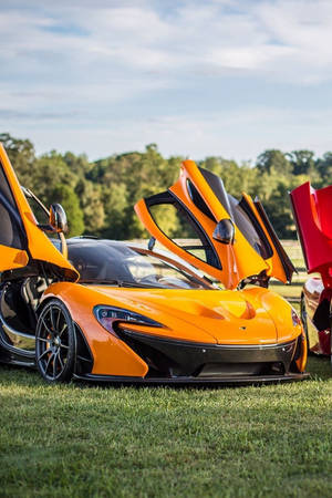 橙色McLaren跑車，鷗翼門打開，停在草地上。 — 麥拉倫 壁紙