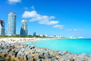 陽光明媚的海灘，碧綠的海水，背景是現代化的城市天際線。 — 海灘 壁紙